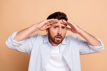 Young man with beard in striped shirt showing shocked expression on beige background