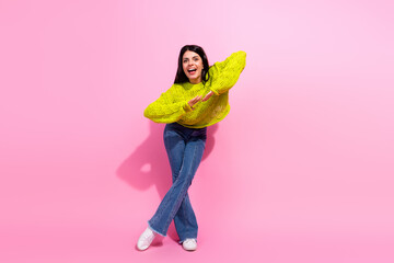 Cheerful young woman in trendy yellow sweater and jeans posing playfully against a vibrant pink...