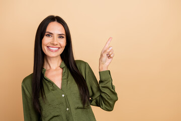 Smiling businesswoman pointing upwards against beige background, wearing stylish green shirt,...