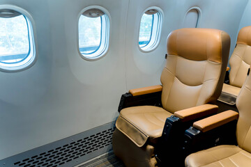 Modern airplane cabin with empty beige leather seats beside window during daytime, comfortable travel and aviation concept interior