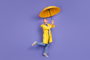 Cheerful senior man holding a yellow umbrella while posing against a vibrant purple background...