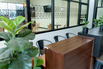Modern waiting area with wooden counter, black chairs, indoor plants, and glass partition wall featuring geometric pattern in a contemporary interior space