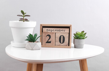 Wooden calendar organizer with date September 20 and decorative plants on table