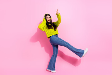 Trendy young woman in vibrant outfit enjoying music and dancing energetically against a pink background