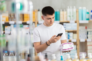 Young male shopper scans QR code on label of feminine pads using her smartphone at small drugstore or hardware store