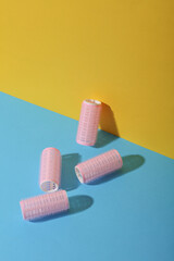 Plastic hair curlers on yellow and blue background. Beauty concept, creative layout