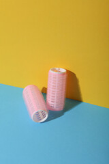 Plastic hair curlers on yellow and blue background. Beauty concept, creative layout