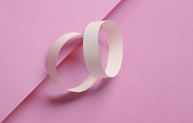Two white paper bracelets on pink background