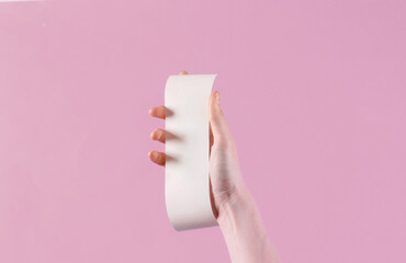 Women's hand hold white empty shopping receipt mockup on pink background. Template for design.