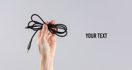 Woman's hand holding usb cable on gray background. Copy space for your text and information