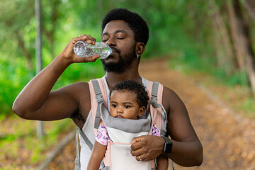 Black father exercising and walking in the park with his daughter in the ergonomic baby carrier. Rio de Janeiro, Brazil.
