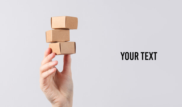 Hand holds a stack of craft boxes, miniature parcels on a gray background. Copy space for your text and information