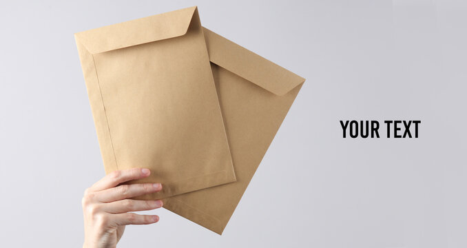 Two craft postal envelopes in  female hand on gray background. Copy space for your text and information
