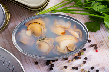 Canned seafood, whole shelled clams served on wooden table with parsley and pepper