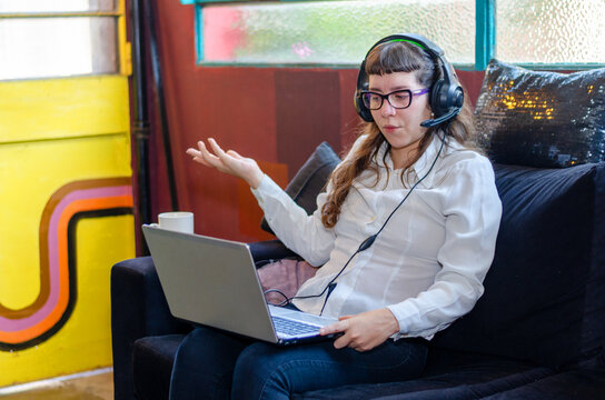 Young woman in headphones talk speak on video call on laptop with client customer. Biracial female have webcam online digital virtual event on computer. Communication concept.