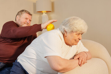 Senior couple using massage ball for back pain relief and wellness therapy at home.