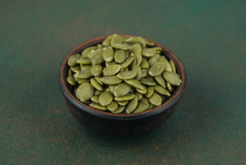 Wooden bowl of pumpkin seeds on green brown background healthy snack