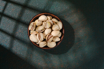 Bowl of pistachios on textured green background healthy snack