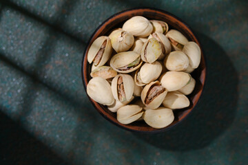 Bowl of pistachios on textured green background healthy snack