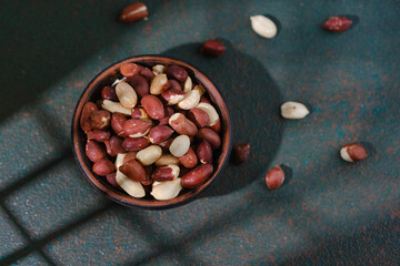 Raw peanuts in wooden bowl on dark green textured background