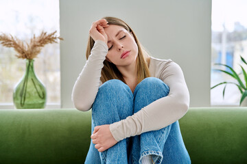 Unhappy upset young woman sitting on sofa at home, face close-up