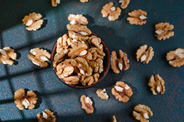 Walnuts in brown wooden bowl with scattered nuts on green textured surface