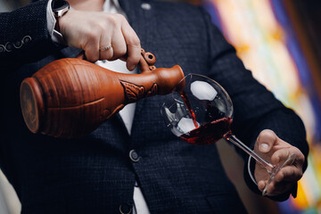Sommelier pouring georgian red wine from clay decanter into glass