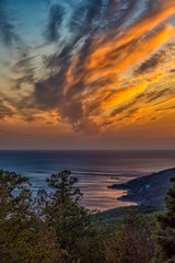 A breathtaking view of the Crimean coast at sunset. From above, a panorama of the Black Sea, coastal hills and pine forest opens up.  