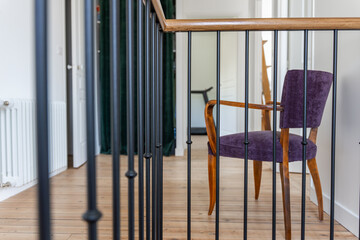 Palier lumineux avec sol en parquet et mobilier moderne, mettant en valeur un fauteuil violet dans...