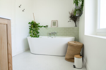 Salle de bain rénovée avec baignoire îlot blanche, carrelage en zellige vert clair, plantes...