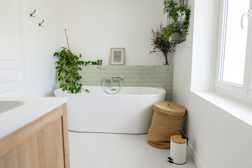 Salle de bain rénovée avec baignoire îlot blanche, carrelage en zellige vert clair, plantes...