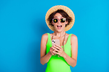 Happy young woman in vibrant summer attire holding phone against bright blue background showcasing a cheerful mood