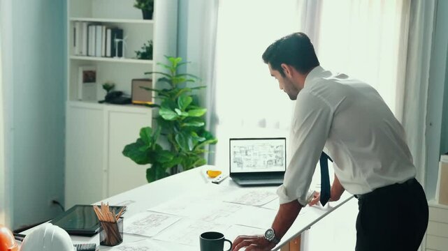 Architect engineer using laptop planning house design at office while sitting at meeting table with blueprint and equipment scatter around.Skilled civil engineer working at blueprint. Alimentation.