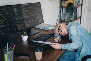 Young professional woman in casual attire visibly exhausted while working on complex programming tasks on dual computer screens in a modern home office setup