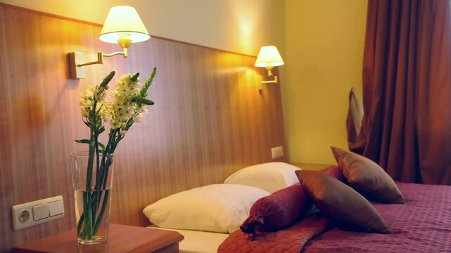 A Chic Hotel Bedroom Decorated in Red Tones. Huge Wooden Headboard. Lit Night Lights. Two White Robes and Slippers on the Bed for a SPA Visit.