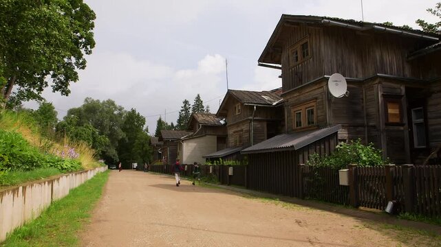 Children are running along a gravel street with old buildings in a small town. A scenic suburban location with ancient, 150-year-old wooden buildings. A pleasant, bright, nostalgic atmosphere.