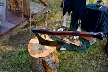 A close up on a massive axe with a wooden handle inserted into a massive log, located next to the replica of a skeleton and other medieval equipment seen in Poland in summer