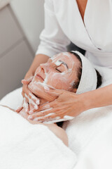 Female beautician applying cleansing foam on mid aged woman face. Cosmetology procedure in beauty clinic. Attractive Young Female Enjoying Skincare Treatments. Soap face clean skin beauty