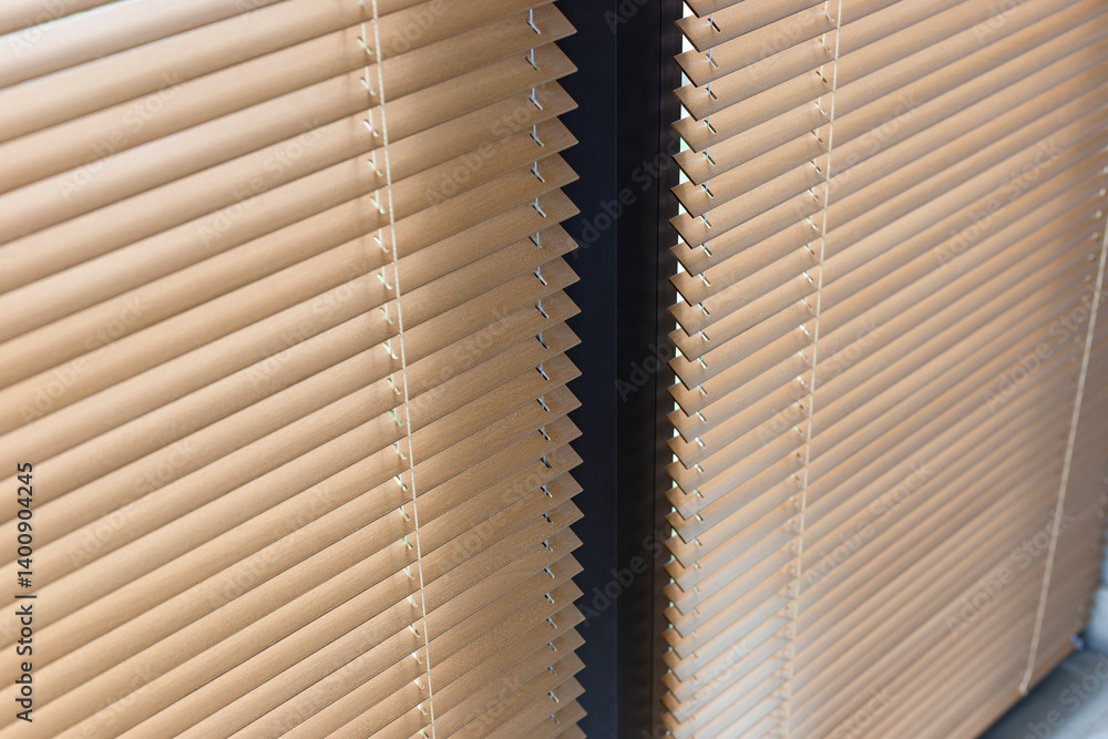 Poster Close-up view of beige horizontal window blinds 25mm, showing the texture and alignment of the wooden slats. Light creates subtle reflections on surface, and dark divider separates two sets of blinds.