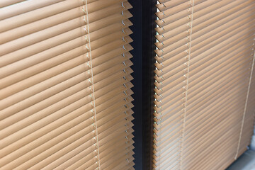 Close-up view of beige horizontal window blinds 25mm, showing the texture and alignment of the wooden slats. Light creates subtle reflections on surface, and dark divider separates two sets of blinds.