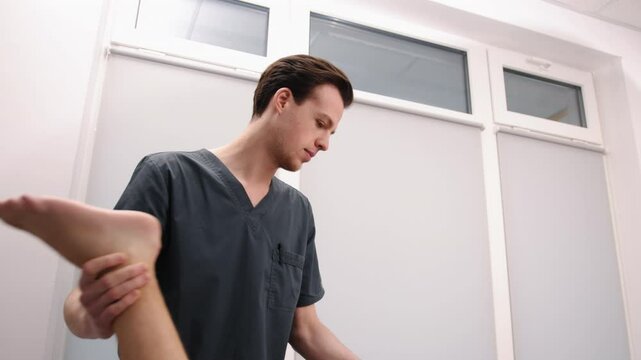 Manual therapy, Chiropractor adjusting, Healthcare session. Wearing dark scrubs, chiropractor performs leg adjustment on male patient who is lying prone on treatment table.