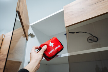 A person is standing and holding a bright red first aid kit firmly in their hand, ready for any...