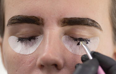 Young woman undergoing procedure of eyelashes dyeing in beauty salon