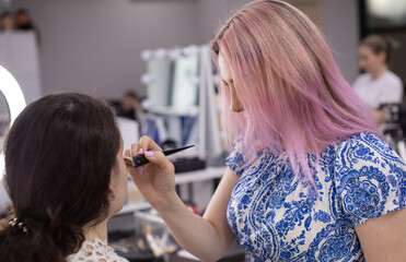 makeup artist applying face powder on beautiful model