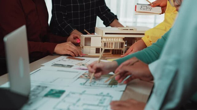 A diverse group of professionals engaged in a lively discussion around architectural blueprints and a scale model, showcasing collaborative design and innovative planning processes. SACTR