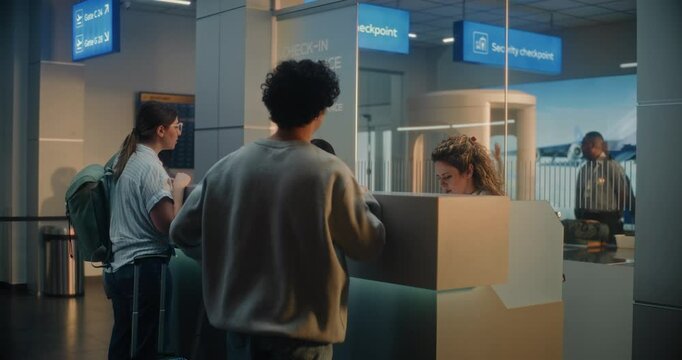 International Airport Terminal: Woman Giving Passport and Flight Ticket for Boarding, Young Man Talking with Female Airline Worker at Airport Check-in Counter. Security Checkpoint in the Background.