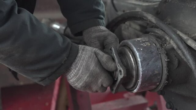 A mechanic in dirty gloves tightens an old nut.
