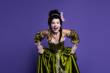 Elegant woman in historic green dress with aristocrat theme posing on purple background