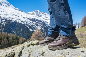 Hiking boots wearing by a man standing on a rock with snowy mountain background