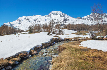 view of snowy alpine mountain with in front a little steam flowing in meadow in the tarentaise valley in Savoie france Le Monal